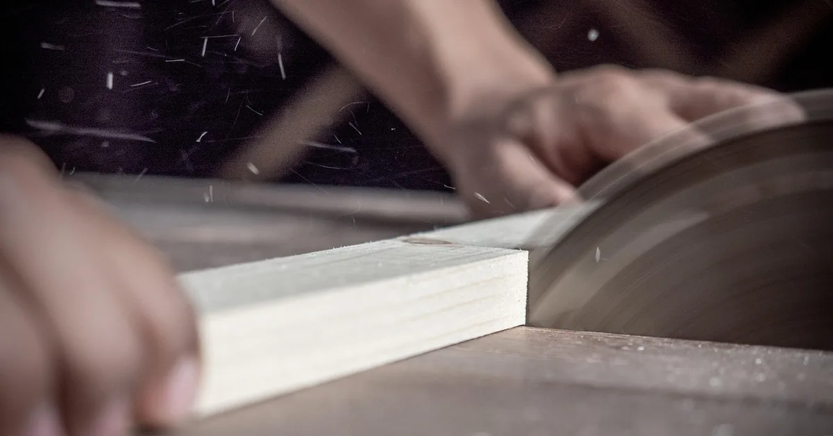 circular saw blade cutting through a wood board with sawdust flying, hands guiding the cut