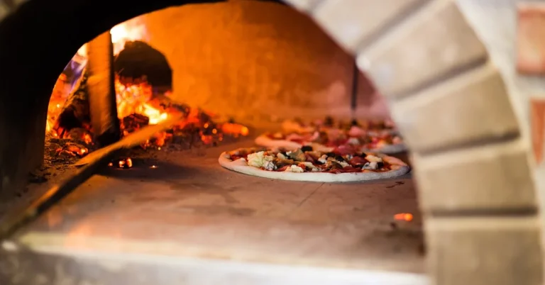 brick wood-fired pizza oven interior with pizzas cooking over open flame