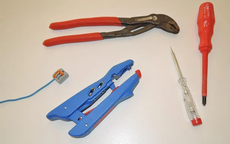 Screwdriver, voltage tester, wire strippers, and pliers laid out for electrical repair work