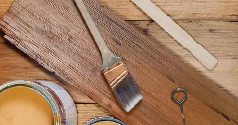 Two open cans of wood stain in different brown tones next to a paintbrush and stir stick on a workbench, ready to blend a custom color