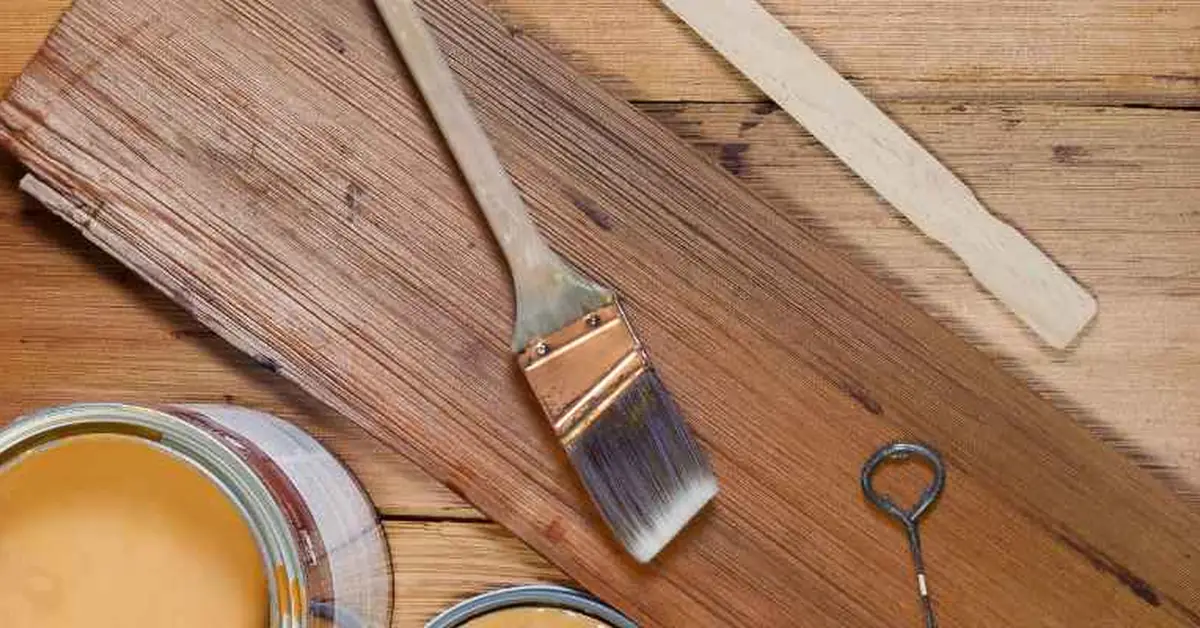 Two open cans of wood stain in different brown tones next to a paintbrush and stir stick on a workbench, ready to blend a custom color