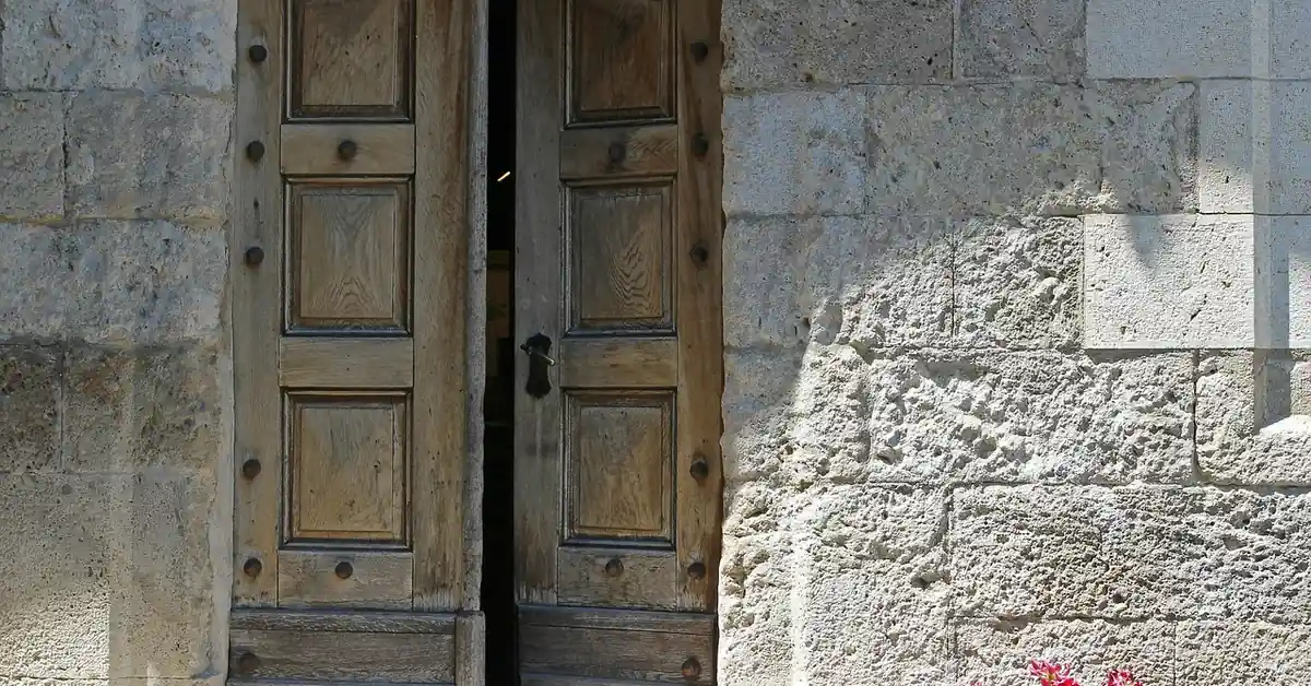 Weathered solid wood double door with visible carved wood door frame in a stone house entrance