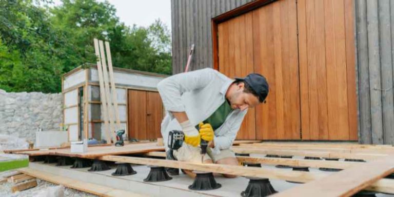 carpenter kneeling and fastening a long deck board across joist supports