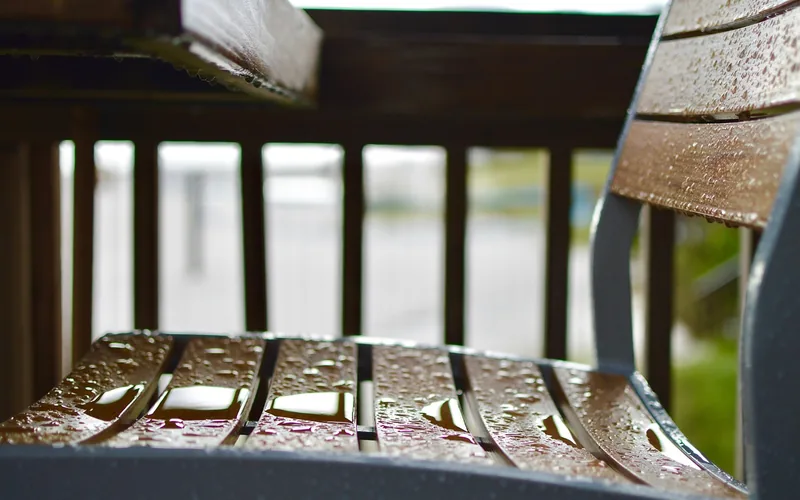 Rain droplets beading on a wooden outdoor chair slat rather than soaking in
