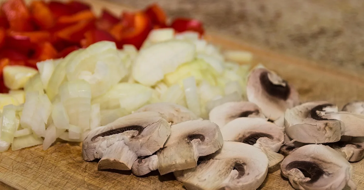 diced vegetables and mushrooms on a wood cutting board showing knife-mark scarring in the surface