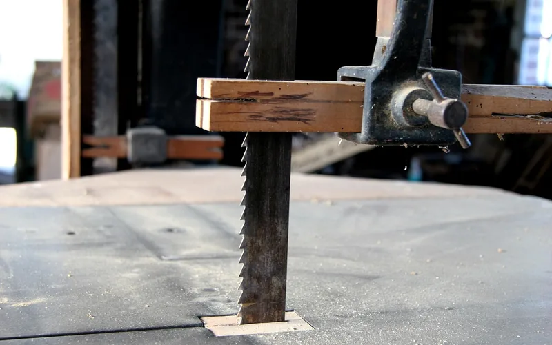 Band saw blade cutting straight down through a clamped wood board