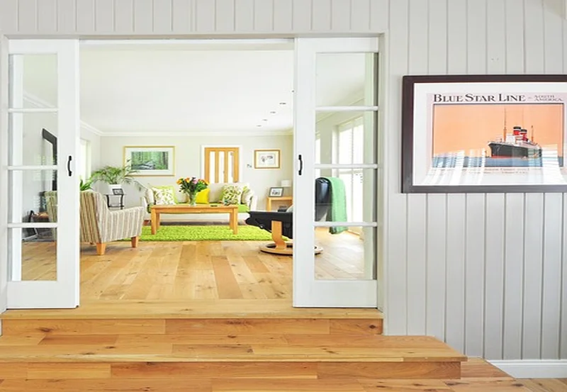 A room entryway with light beige wood flooring transitioning from a wood step into a living area