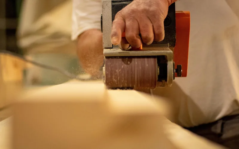 belt sander with visible sanding belt removing material from a wood plank, sawdust flying belt sander with visible sanding belt removing material from a wood plank, sawdust flying