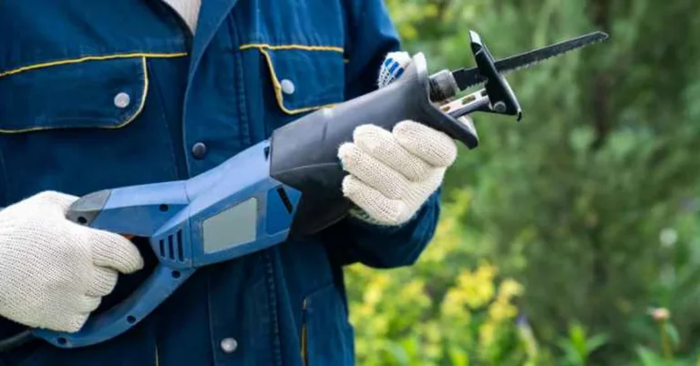 A cordless reciprocating saw fitted with a pruning blade, held by a gloved worker outdoors