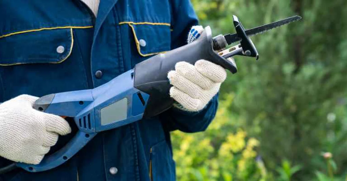 A cordless reciprocating saw fitted with a pruning blade, held by a gloved worker outdoors