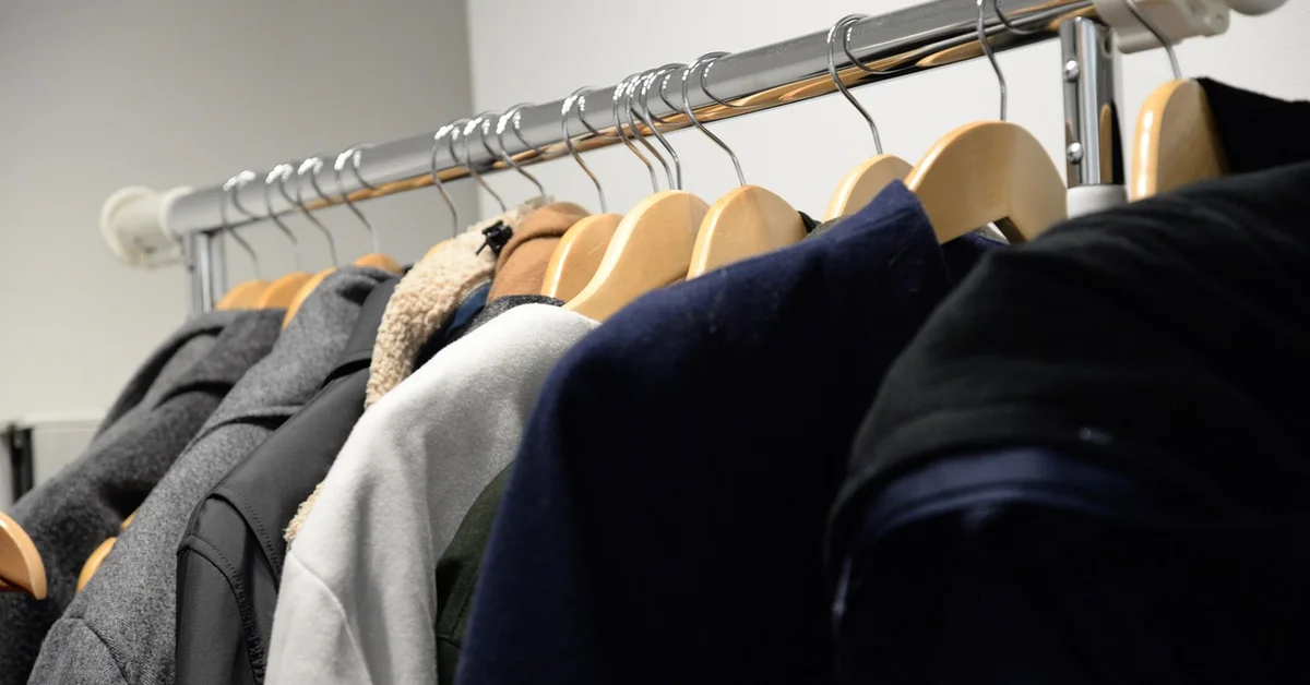 Real wooden coat hangers with contoured shoulders holding jackets and coats on a closet rail