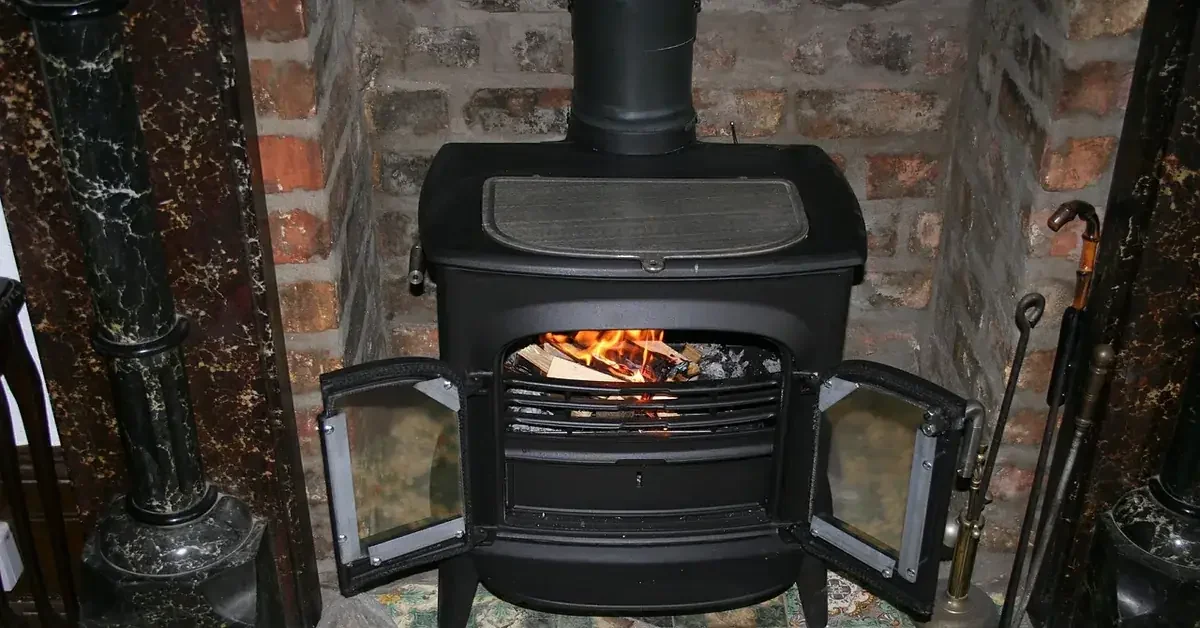 Black freestanding wood stove with a stove pipe rising from the top, set in a brick alcove