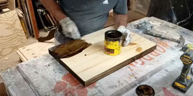 person brushing dark wood stain onto a pine board