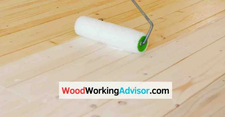 Paint roller applying white floor paint to a bare wood floor