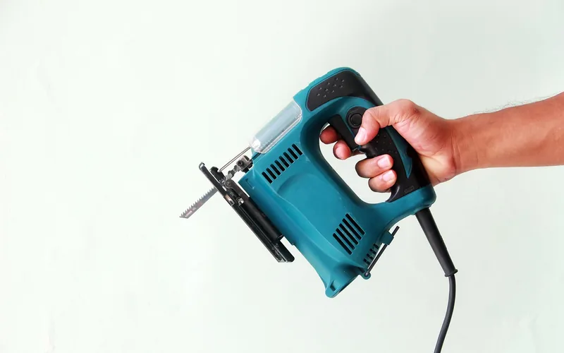hand holding a corded jigsaw with blade extended before cutting a board