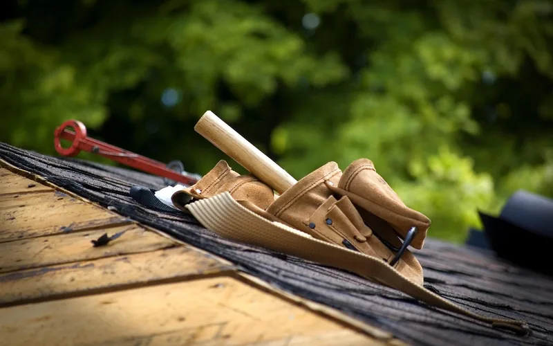Carpenter tool belt with hammer resting on a wood shingle roof during a siding repair job