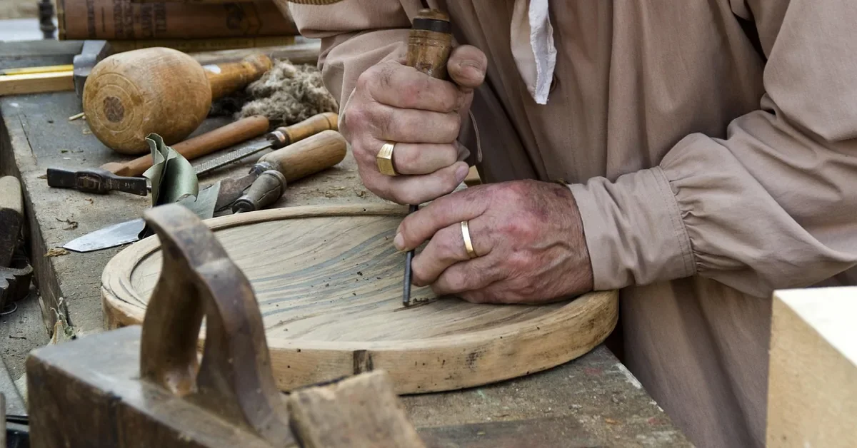 Woodworker hand carving a shallow wooden dish with a gouge at a workbench