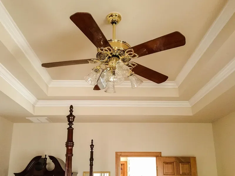 Ceiling fan with walnut-finish wooden blades and a light kit mounted in a tray ceiling Ceiling fan with walnut-finish wooden blades and a light kit mounted in a tray ceiling