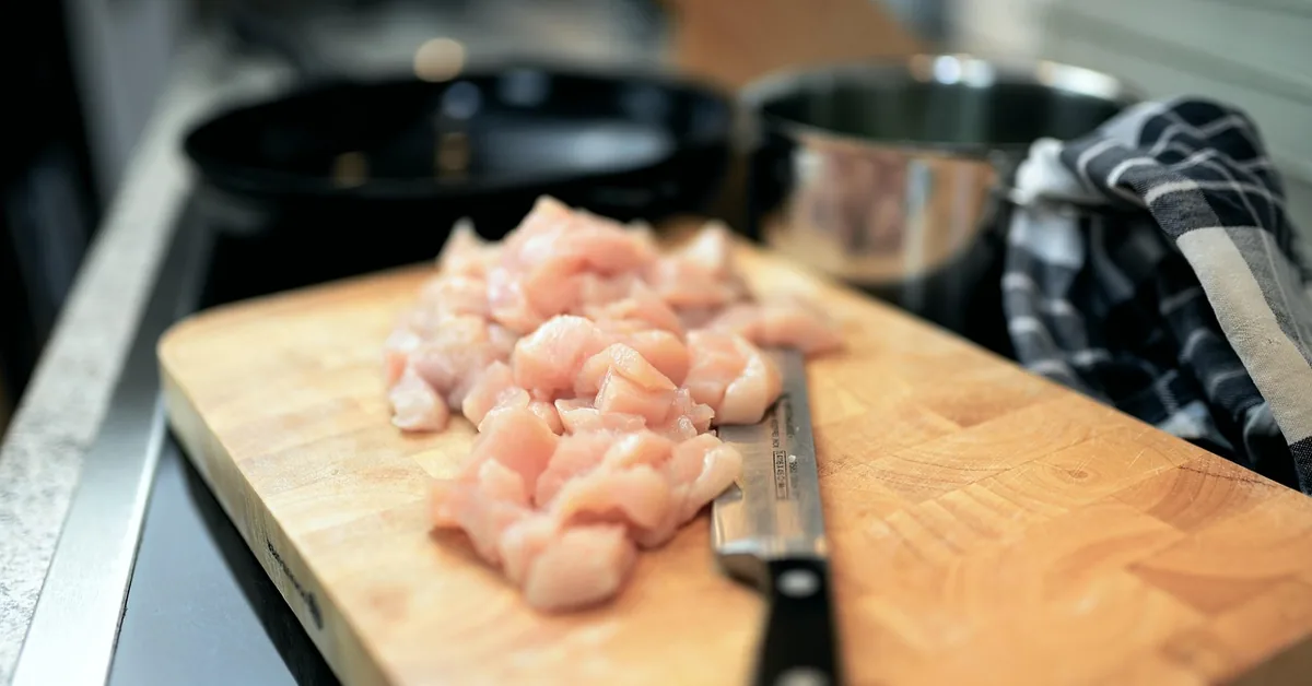 raw chicken pieces sliced with a knife on a wood cutting board