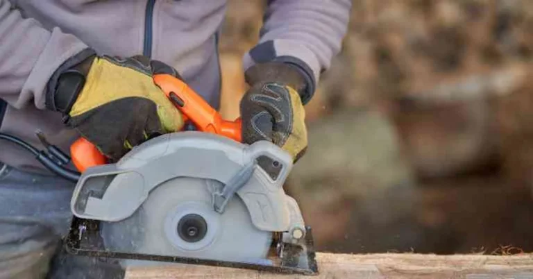 gloved hands guiding a handheld circular saw through a board outdoors