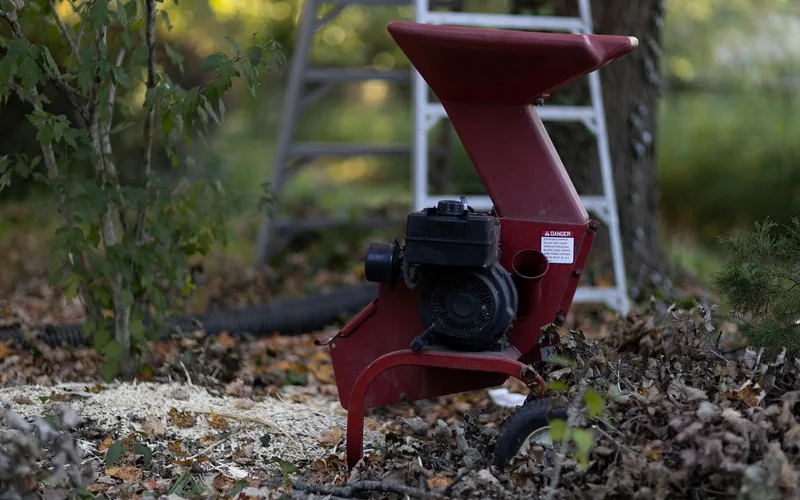 small gas wood chipper shredding branches beside a leaf pile in a backyard small gas wood chipper shredding branches beside a leaf pile in a backyard