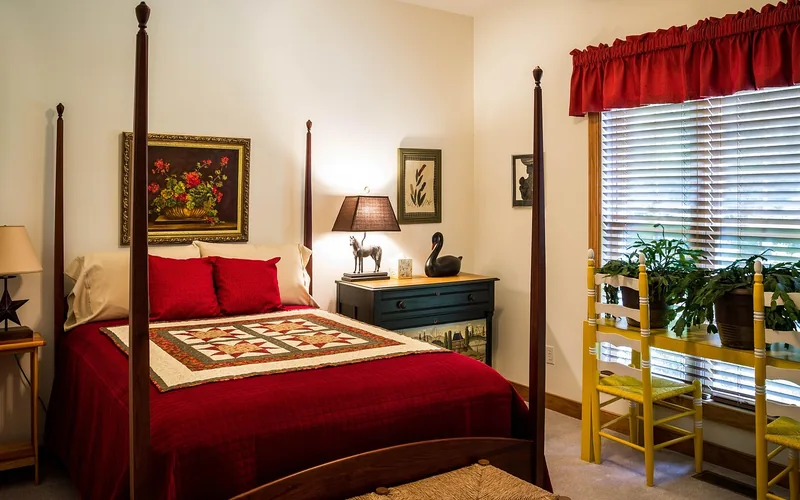 dark mahogany four-poster bed frame with cream walls and deep red bedding