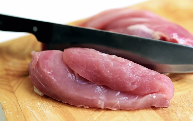 diced raw chicken on a wood cutting board next to kitchen pans diced raw chicken on a wood cutting board next to kitchen pans