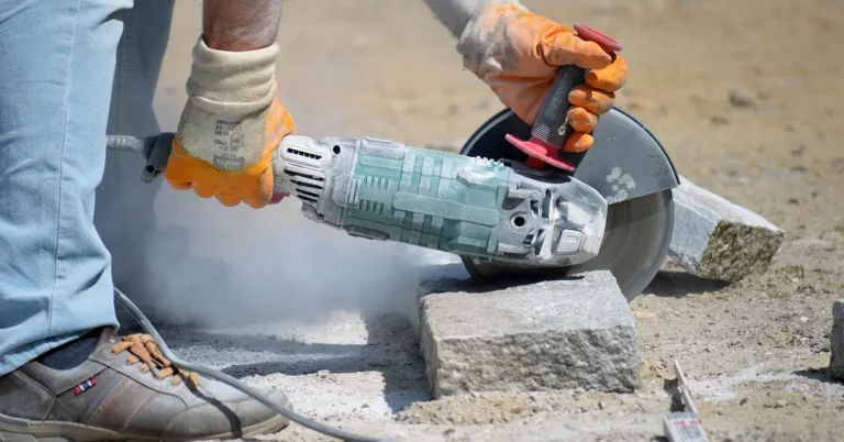 Angle grinder with a diamond-style cutting disc slicing through granite pavers outdoors