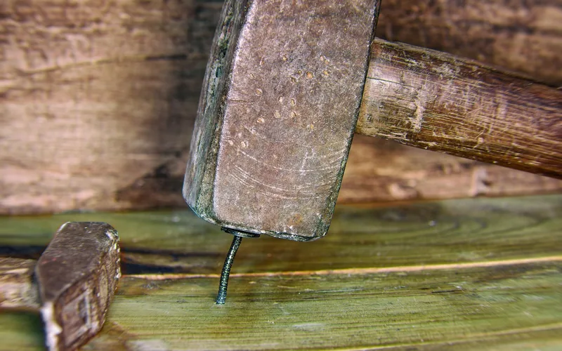 hammer driving a nail into a hardwood flooring board during installation