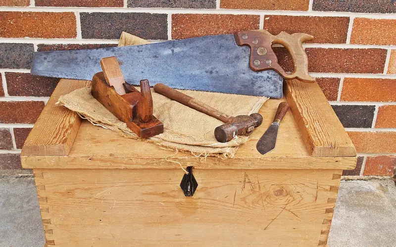 hand saw, hand plane, hammer and marking knife laid on an old wooden tool chest