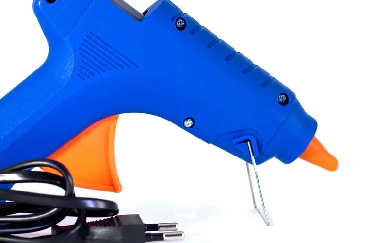 Close-up of a hot glue gun trigger, nozzle, and support stand Close-up of a hot glue gun trigger, nozzle, and support stand