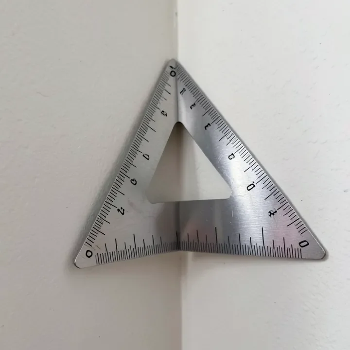 Speed square checking a wall corner angle before cutting baseboard