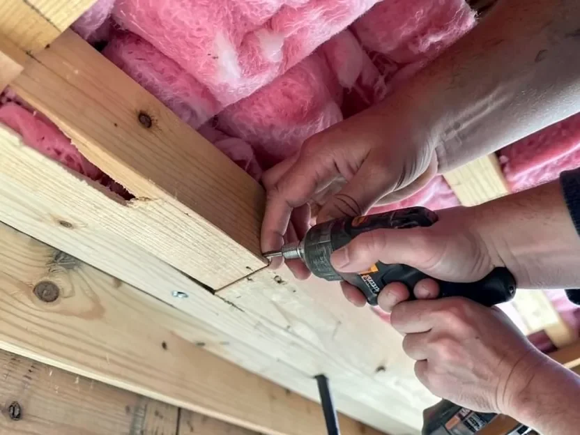 Installing plywood attic flooring screwing a plywood floor panel into an attic ceiling joist