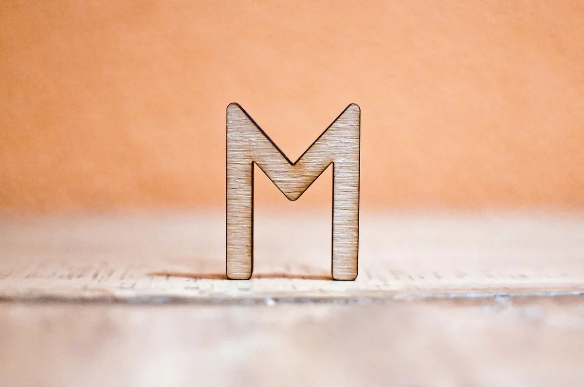 A laser-cut plywood letter standing on a wooden surface