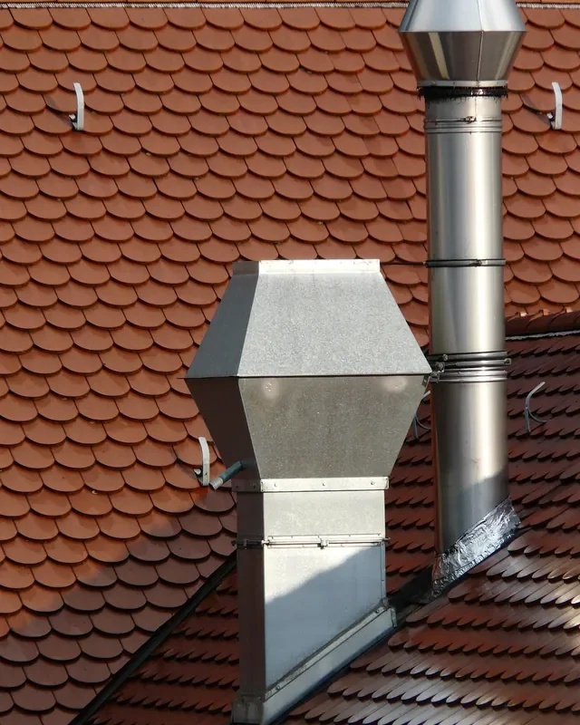 Stainless steel chimney pipe rising above a terracotta tile roof next to a galvanized hood