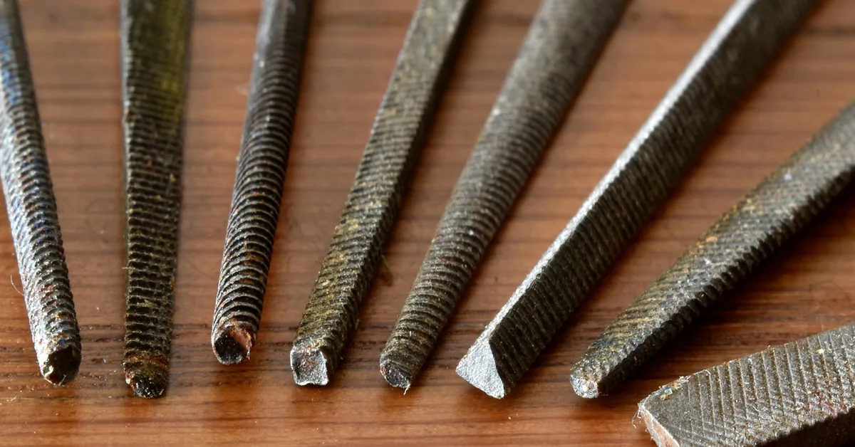 assorted metal files with different tip shapes and cuts laid out on a workbench