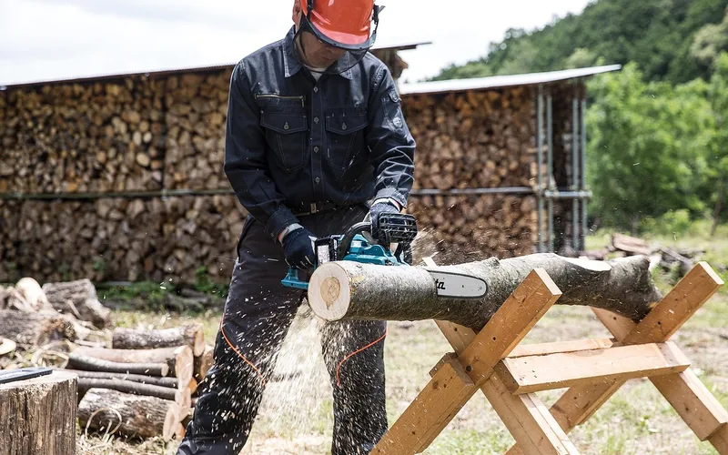 chainsaw operator wearing helmet and gloves cutting a log on a sawhorse