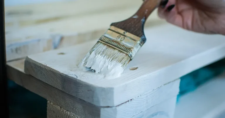 Brush applying white acrylic latex paint to interior wood trim