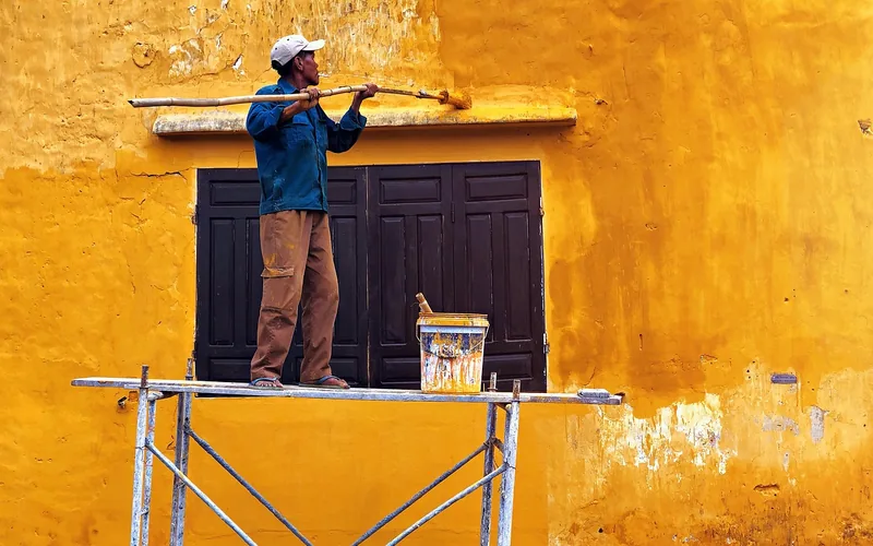 Painter coating an exterior wall and window frame with weather-resistant paint