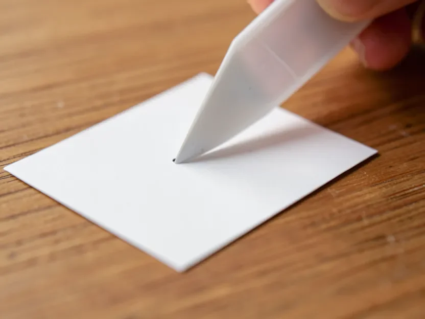Using a plastic scraper to gently lift a sticker off wood at a low angle