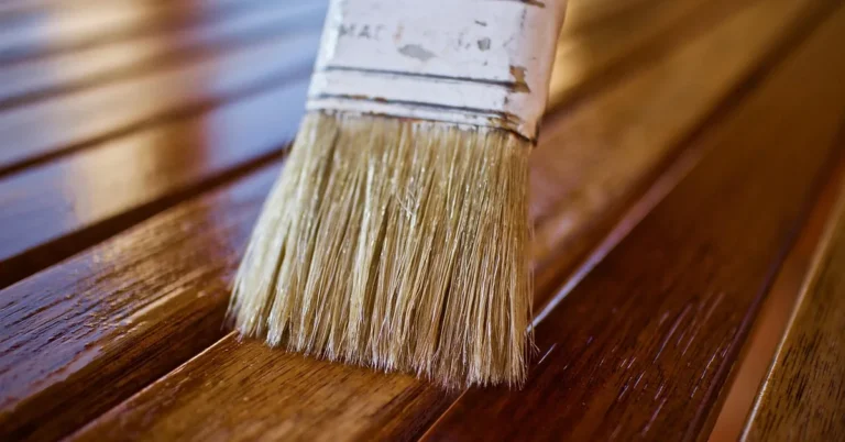 Natural bristle brush applying polyurethane finish to a wood board