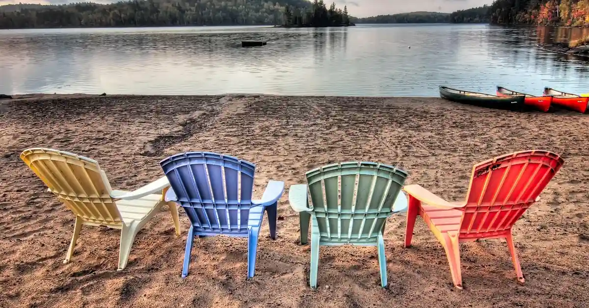 colorful weatherproof Adirondack chairs on a sandy patio near water