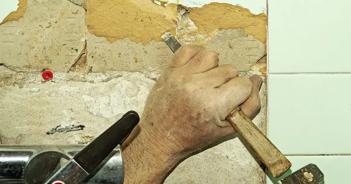 Using a hammer and chisel to break up old glued-down flooring adhesive during removal