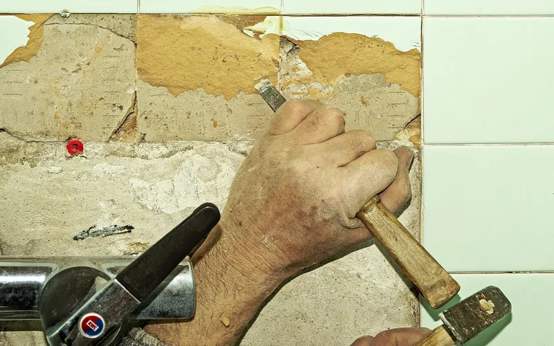worker chiseling old tile flooring off a subfloor before new vinyl plank installation worker chiseling old tile flooring off a subfloor before new vinyl plank installation