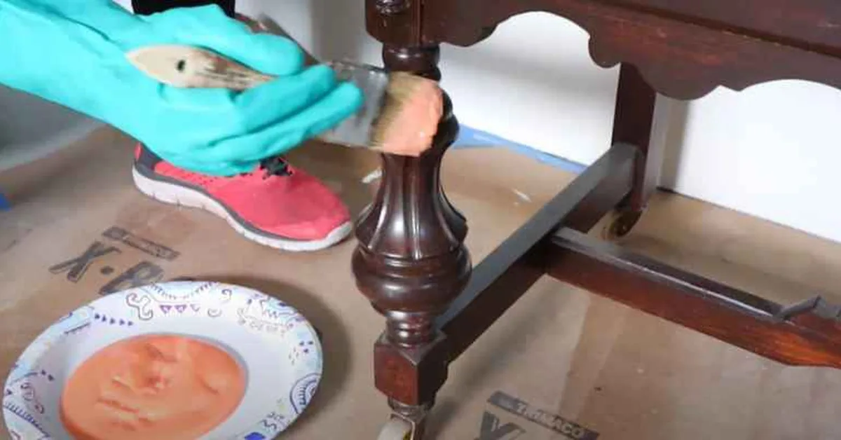Removing dried paint splatter from a dark-stained wooden furniture leg with a cloth