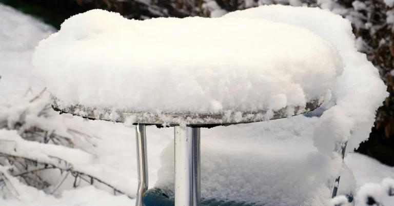 Outdoor patio table and chair set fully covered with a fitted cover during snowfall