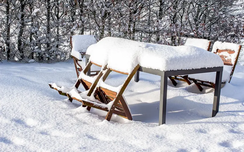 Uncovered patio table and chairs exposed to fresh snowfall in a backyard
