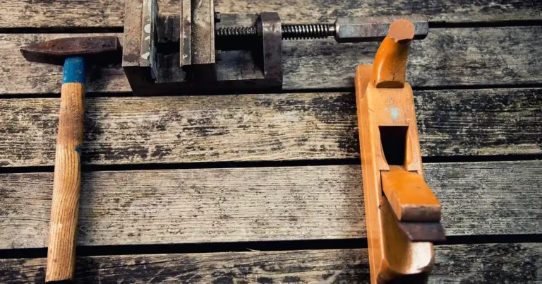 carpentry hand tools including a hammer, clamp, and wood plane laid on a wooden plank surface