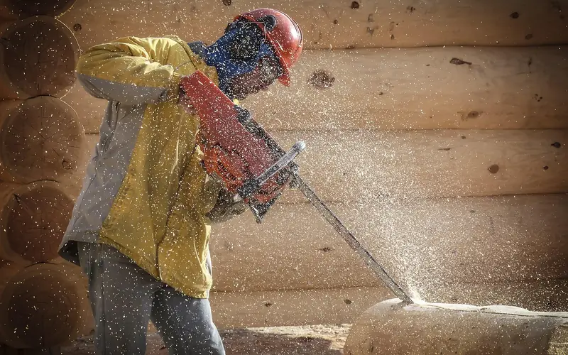 carpenter using a gas chainsaw to trim a log during log-cabin construction carpenter using a gas chainsaw to trim a log during log-cabin construction