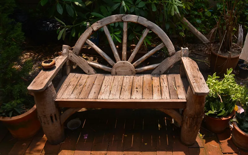 weathered wood garden bench with wagon-wheel design sitting outdoors among potted plants